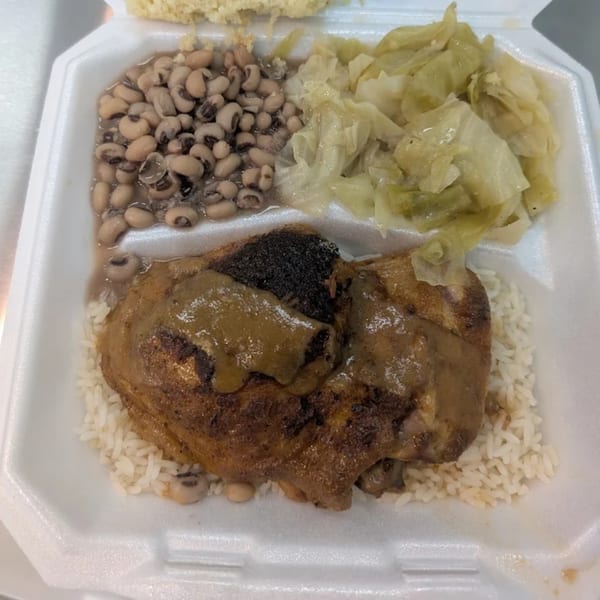Soul food meal with black-eyed peas, cabbage, gravy-covered chicken, and rice in a takeout container.