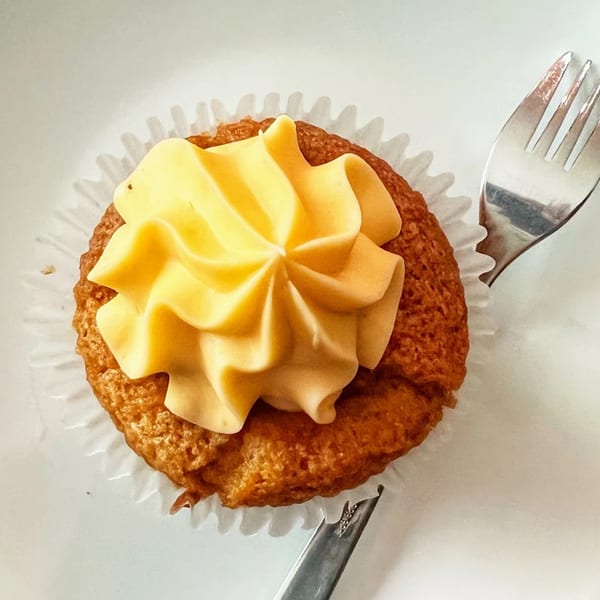 A Timeless Treat cupcake with yellow frosting and a fork on a white plate.