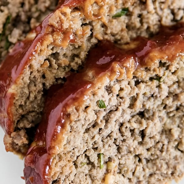 Close-up of sliced meatloaf with a rich, glossy tomato glaze, showcasing its texture.